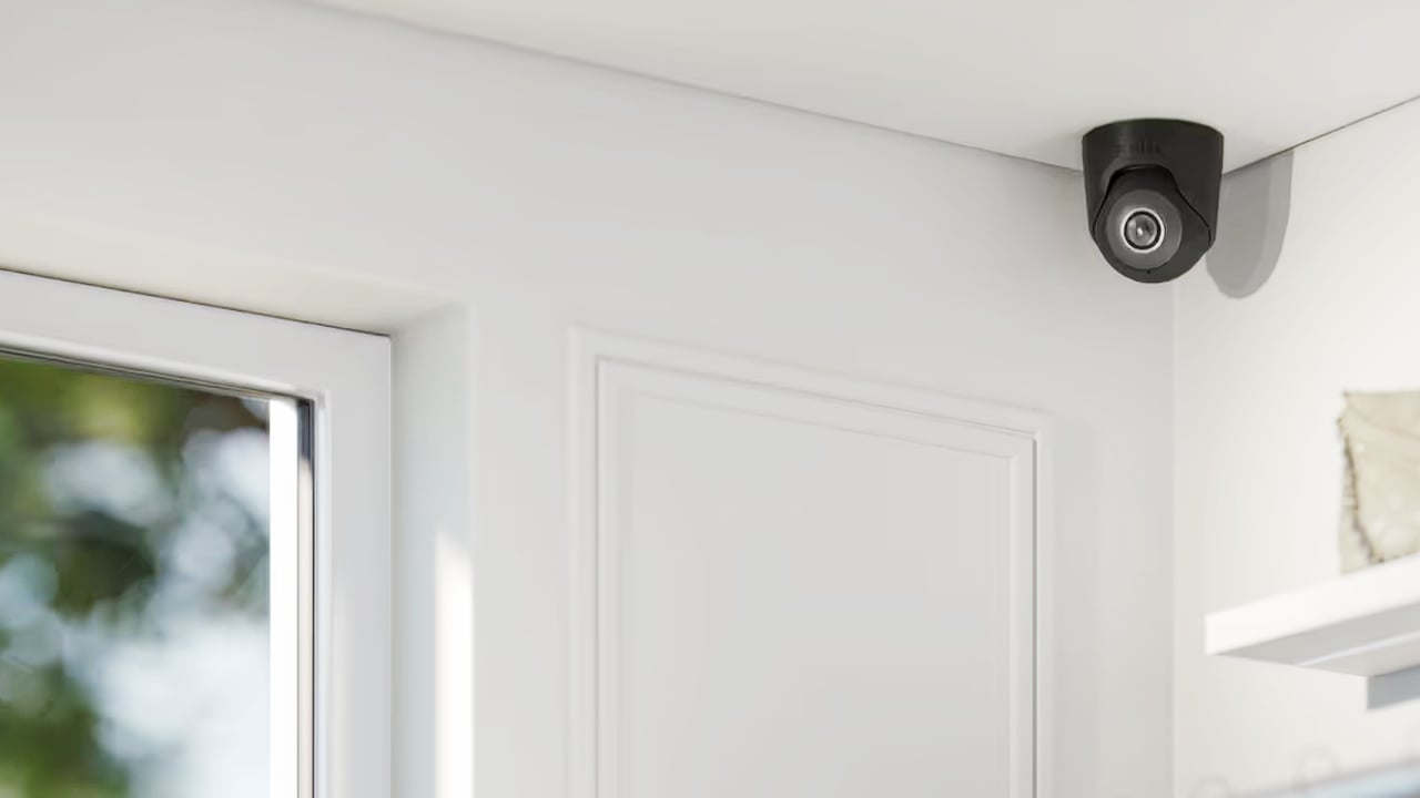 A compact dome CCTV camera mounted near the ceiling corner of a bright interior.