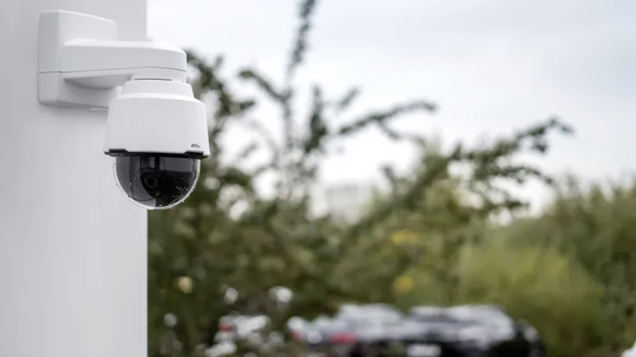 Flexible for Homes & Businesses - Axis PTZ Outdoor Security Camera – Wide-Area Surveillance in Brisbane Axis PTZ outdoor security camera mounted on a white wall in Brisbane with trees and parked cars in the background.